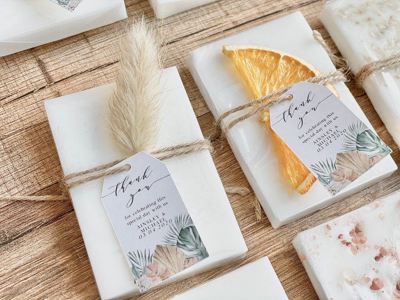 May include: White favour boxes with a thank you tag, a dried orange slice, and a sprig of pampas grass. The tag says "thank you for celebrating this special day with us Ainsley & Michael 03.04.2020".