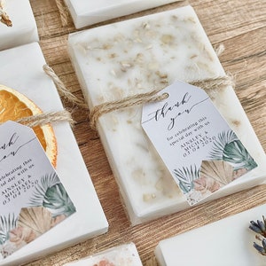 May include: White square boxes containing a white soap bar, tied with twine and a small tag. The tag features a tropical leaf design and the text "Thank you for celebrating this special day with us Ainsley & Michael 03.04.2020".