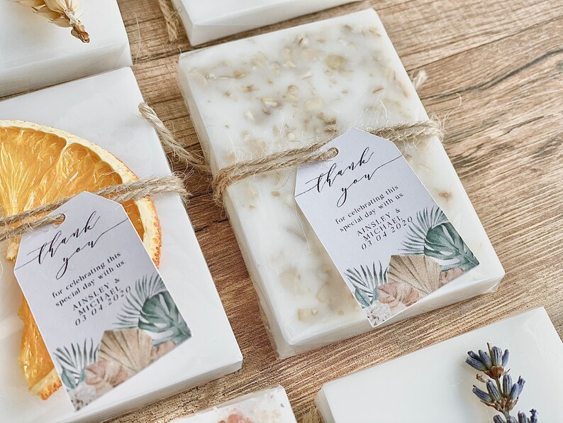 May include: White square boxes containing a white soap bar, tied with twine and a small tag. The tag features a tropical leaf design and the text "Thank you for celebrating this special day with us Ainsley & Michael 03.04.2020".