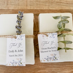 May include: Two white soap bars with floral-patterned thank you tags. One tag says "Thank You Emily & John March 31st, 2024" and the other says "Thank You From Rachel's Shower to Yours".