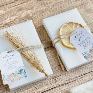 May include: Two white boxes with thank you tags tied with twine. One box has a dried lemon slice and the other has a wheat stalk. The tags have a floral design and the text "thank you for celebrating this special day with us AINSLEY & MICHAEL 01.04.2020".
