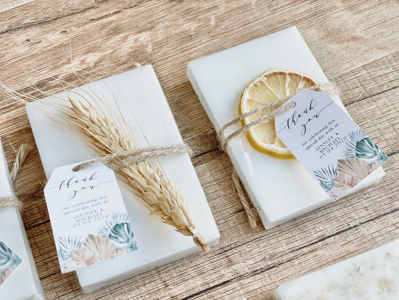 May include: Two white boxes with thank you tags tied with twine. One box has a dried lemon slice and the other has a wheat stalk. The tags have a floral design and the text "thank you for celebrating this special day with us AINSLEY & MICHAEL 01.04.2020".