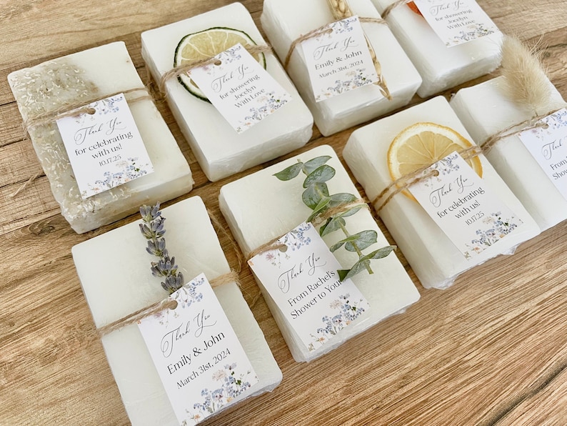 May include: A collection of small white soap bars wrapped in twine and decorated with dried flowers, herbs, and citrus slices. Each bar has a small thank you tag with a floral design and personalized text.