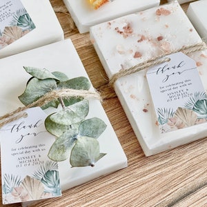 May include: White soap bars with a natural, earthy theme. Each bar is wrapped with twine and decorated with dried eucalyptus leaves and a small tag that says "Thank you for celebrating this special day with us Ainsley & Michael 03.04.2020".