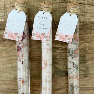 May include: Three glass test tubes with cork tops and twine tied around the tops. Each tube contains bath salts and has a tag attached. The tags are white with pink hearts and the text "Happy Valentine's Day" and "Happy Valentine's Day, Love, Courtney".
