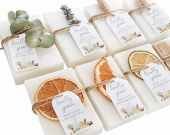 May include: A collection of rectangular white soap bars, each wrapped in twine and adorned with a tag reading locally grown thank you for celebrating with us. Some bars feature dried orange slices, lavender sprigs, or green eucalyptus leaves.