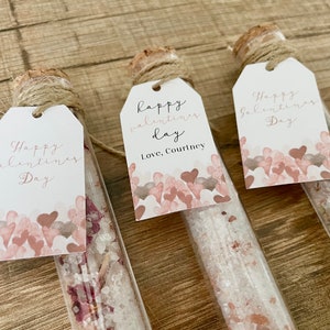 May include: Three glass test tubes filled with bath salts and dried flowers, each with a small white tag tied with twine. The tags have handwritten messages that say "Happy Valentine's Day" and "Happy Valentine's Day, Love, Courtney".