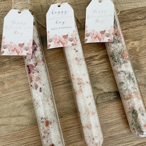 May include: Three glass test tubes filled with bath salts and dried flowers. Each tube has a tag tied around the top with the text "Happy Valentine's Day" and a pink and white heart pattern. One tag also includes the text "Love, Courtney".