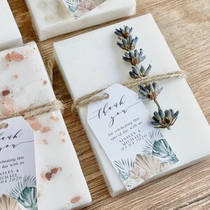 May include: White favour boxes with a floral design and the text "thank you for celebrating this special day with us Ainsley & Michael 03.04.2020". The boxes are tied with twine and decorated with dried lavender.
