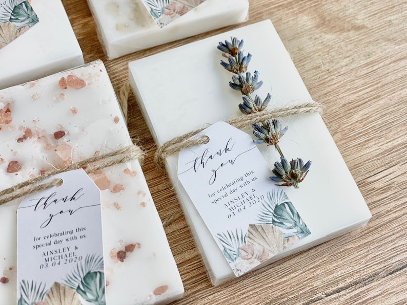May include: White favour boxes with a floral design and the text "thank you for celebrating this special day with us Ainsley & Michael 03.04.2020". The boxes are tied with twine and decorated with dried lavender.
