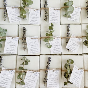 May include: A collection of small white soap bars wrapped in twine and decorated with sprigs of eucalyptus and lavender. Each bar has a small tag attached that reads "Thank You for celebrating with us! Baby Lentz Baby Shower March 16, 2024".