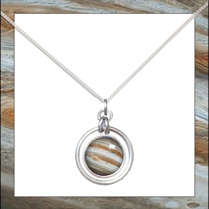 Puede incluir: Un collar de cadena de plata con un colgante redondo que presenta una imagen detallada de Júpiter. El colgante tiene un anillo de plata alrededor de la imagen.