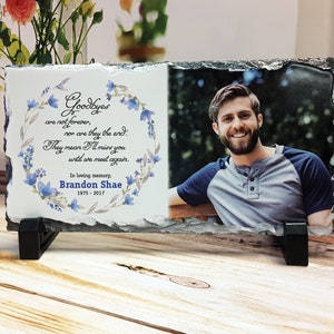 May include: A white slate memorial plaque with a floral wreath design and a photo of a man. The plaque reads "Goodbyes are not forever, nor are they the end. They mean I'll miss you until we meet again. In loving memory, Brandon Shae 1975-2017."