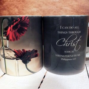 May include: Two black ceramic mugs with white handles. One mug features a red flower in a glass bottle and the other mug has the text "I can do all things through Christ which strengtheneth me. Philippians 4:13".