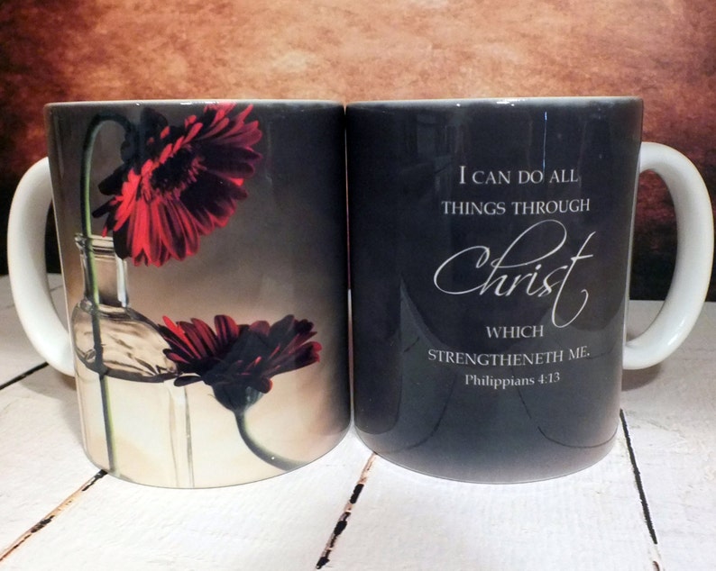 May include: Two black ceramic mugs with white handles. One mug features a red flower in a glass bottle and the other mug has the text "I can do all things through Christ which strengtheneth me. Philippians 4:13".