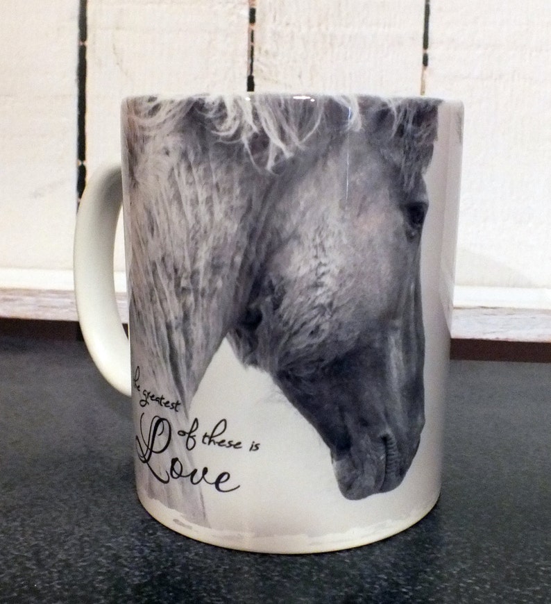 May include: White ceramic mug with a black and white photo of a horse's head. The text "The greatest of these is Love" is printed on the mug.