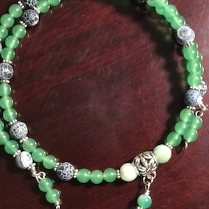 May include: A double-strand necklace with green and gray beads. The necklace has a silver clasp and a silver pendant with a floral design.