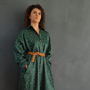May include: A green shirt dress with a small yellow floral pattern and a brown belt. The dress is worn with matching green pants and beige woven sandals.