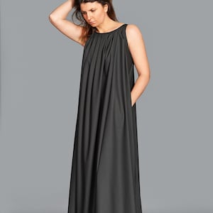 May include: A sleeveless, floor-length black dress with a pleated bodice and side pockets. The dress has a simple, elegant design, suitable for various occasions. The model is wearing light pink shoes.
