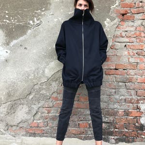 May include: A black zip-up jacket with a high collar and a relaxed fit. The jacket is worn with black jeans and pink sneakers.