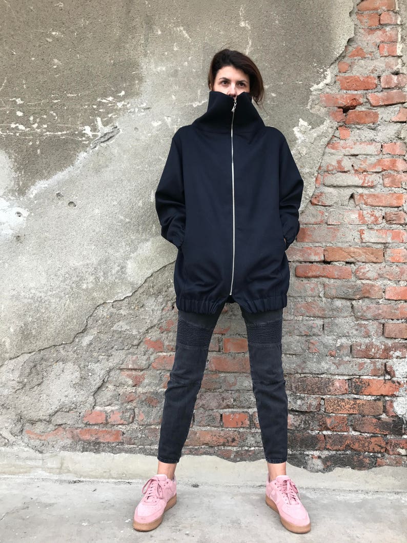 May include: A black zip-up jacket with a high collar and a relaxed fit. The jacket is worn with black jeans and pink sneakers.