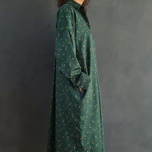 May include: A long, green shirt dress with a small yellow floral pattern. The dress has a collared neckline and long sleeves. The model is wearing the dress with matching pants and beige woven sandals.