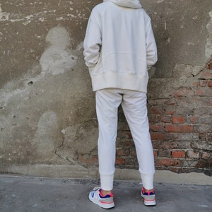 May include: A white hooded sweatshirt and matching sweatpants with a white drawstring. The person is wearing white sneakers with blue and pink accents.