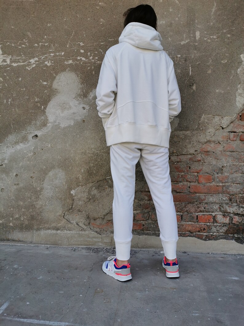 May include: A white hooded sweatshirt and matching sweatpants with a white drawstring. The person is wearing white sneakers with blue and pink accents.