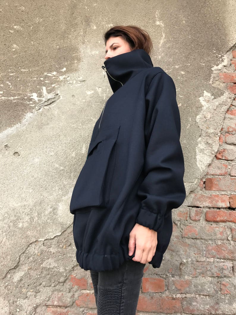 May include: A navy blue oversized jacket with a high collar and a zipper closure. The jacket has a large pocket on the front and a drawstring at the bottom.
