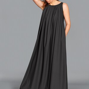 May include: A sleeveless, floor-length black dress with a pleated bodice. The dress has a flowing, A-line skirt and is worn with light pink sneakers. The model is standing against a gray background.