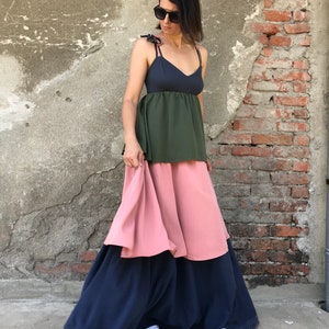 May include: A woman wearing a layered dress with a dark blue top, a green middle layer, and a pink bottom layer. The dress has thin straps and a loose fit. She is wearing white sneakers.