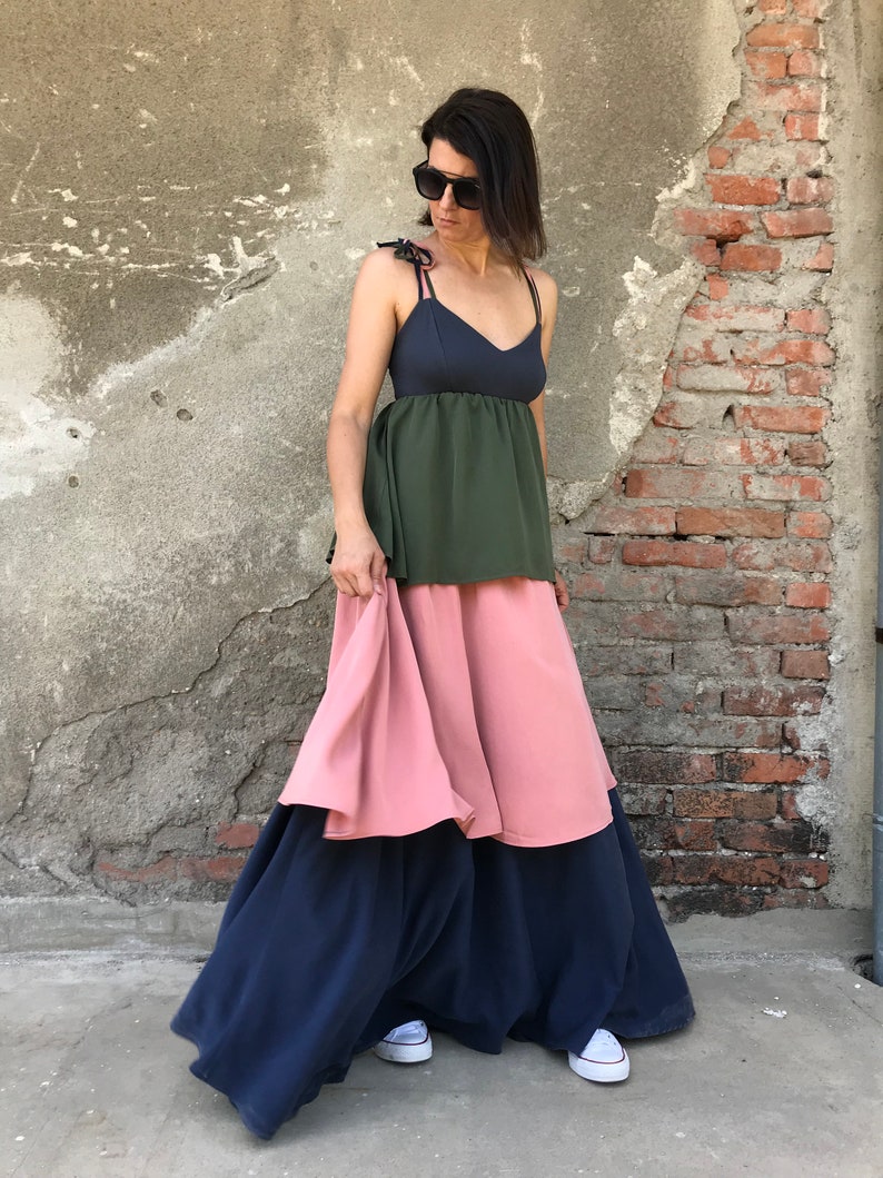 May include: A woman wearing a layered dress with a dark blue top, a green middle layer, and a pink bottom layer. The dress has thin straps and a loose fit. She is wearing white sneakers.