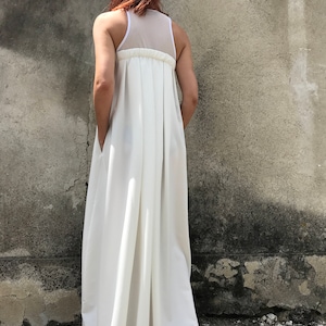 May include: A white maxi dress with a sheer mesh panel on the back. The dress has a gathered waist and a flowing skirt.