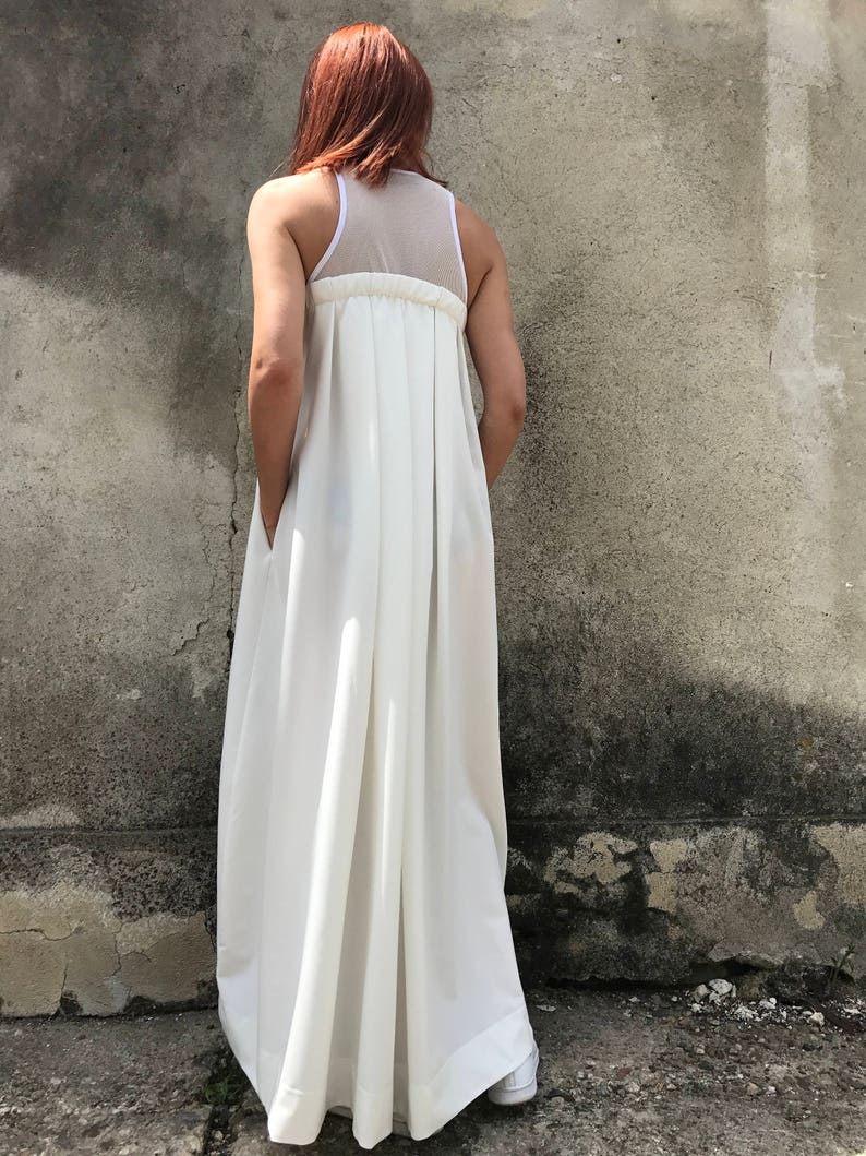 May include: A white maxi dress with a sheer mesh panel on the back. The dress has a gathered waist and a flowing skirt.