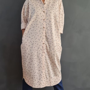 May include: A long-sleeved, pink button-down shirt with a small, dark blue print. The shirt is worn with dark blue pants and beige sandals.
