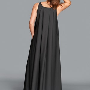 May include: A black sleeveless maxi dress with a pleated bodice and a flowing skirt. The dress has a scoop neckline and pockets. The model is wearing the dress and has their hand in their hair.