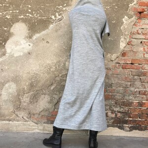 May include: A long, gray, hooded dress with a loose fit. The dress is made of a soft, comfortable fabric and has a relaxed, casual style. The model is wearing black boots.