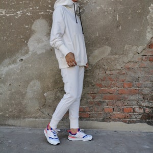 May include: A white hooded sweatshirt and matching sweatpants with a pair of white sneakers with pink and blue accents.