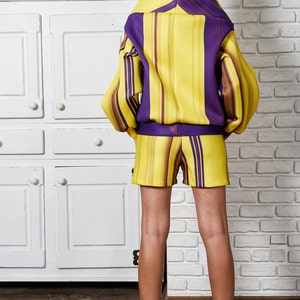 Puede incluir: Un conjunto de short amarillo y morado a rayas con una parte superior de cuello alto de manga larga y shorts a juego. La modelo lleva botas marrones.