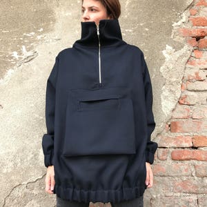 May include: A navy blue oversized pullover with a high mock neck, a zipper closure, and a large patch pocket on the front. The pullover has a drawstring at the bottom.