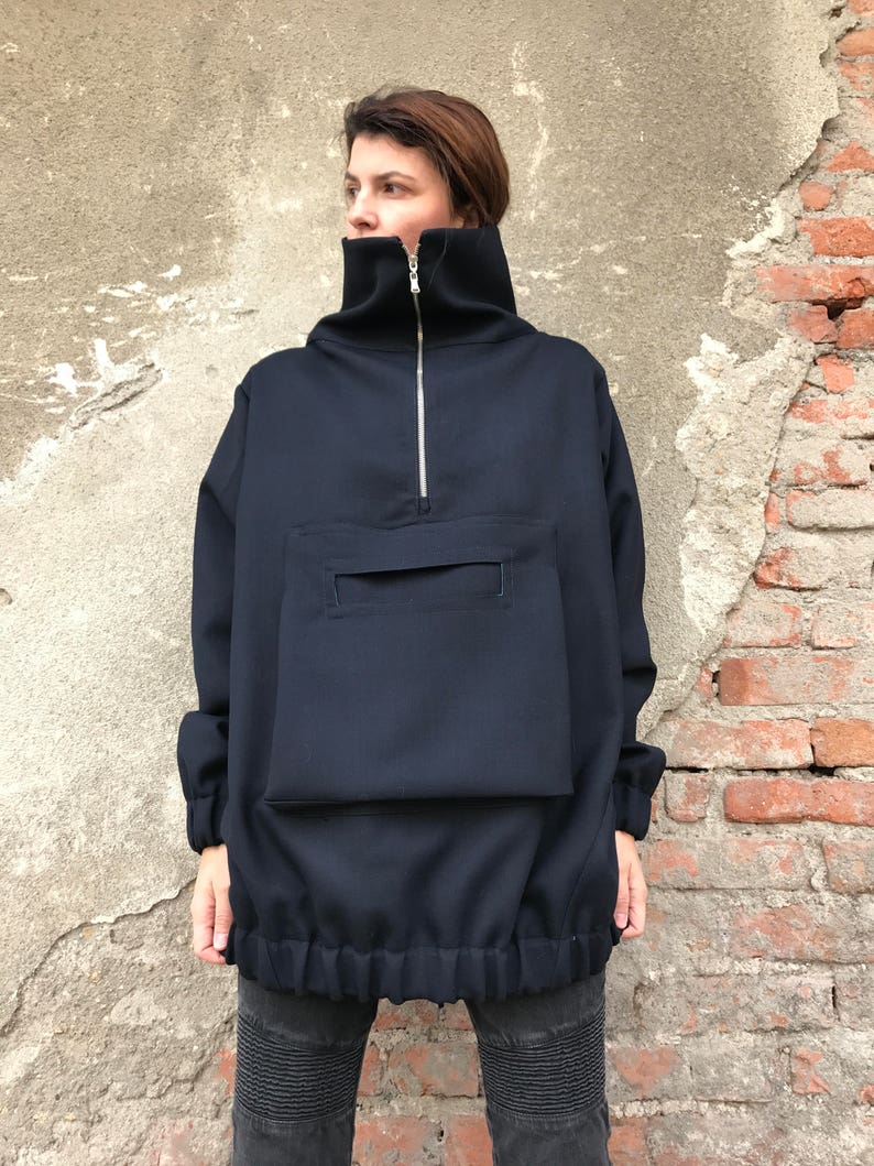 May include: A navy blue oversized pullover with a high mock neck, a zipper closure, and a large patch pocket on the front. The pullover has a drawstring at the bottom.