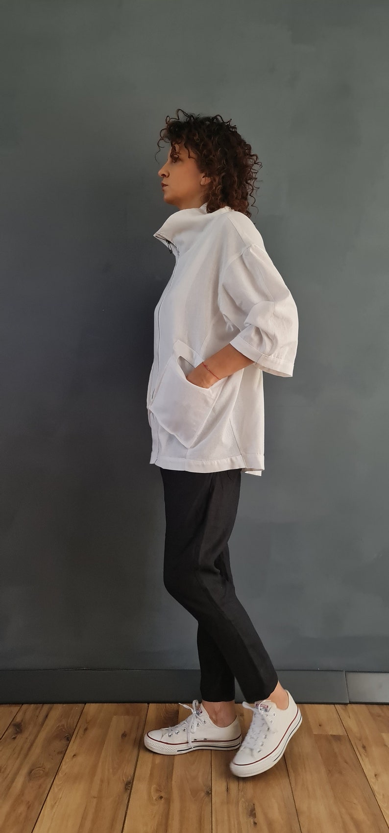 May include: A white collared shirt with a zipper closure and a large pocket on the front. The shirt is worn with black pants and white sneakers.