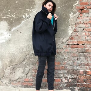May include: A navy blue oversized zip-up jacket with a high collar and a drawstring at the waist. The jacket is worn with black pants and pink sneakers.