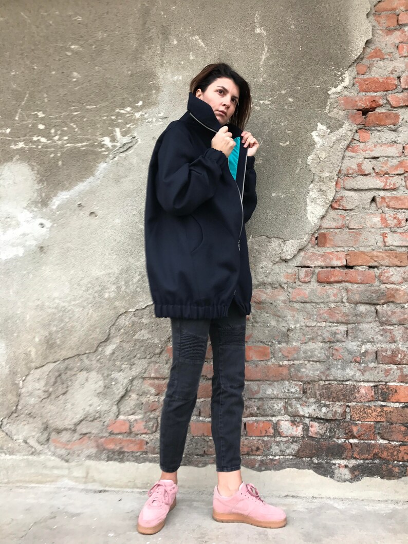 May include: A navy blue oversized zip-up jacket with a high collar and a drawstring at the waist. The jacket is worn with black pants and pink sneakers.