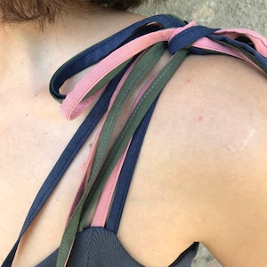 May include: A dark blue tank top with three straps, one pink, one dark green, and one navy blue, tied together at the shoulder.