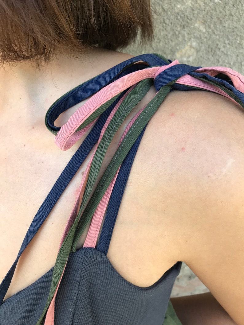 May include: A dark blue tank top with three straps, one pink, one dark green, and one navy blue, tied together at the shoulder.