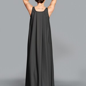 May include: A long, dark gray maxi dress with a simple, sleeveless design. The dress features a square neckline and a flowing, floor-length skirt. The model's arms are raised, and the back of the dress is visible.