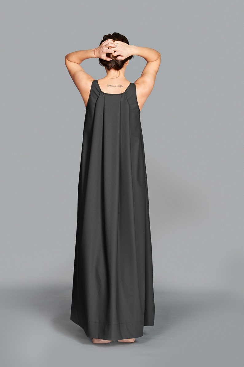 May include: A long, dark gray maxi dress with a simple, sleeveless design. The dress features a square neckline and a flowing, floor-length skirt. The model's arms are raised, and the back of the dress is visible.