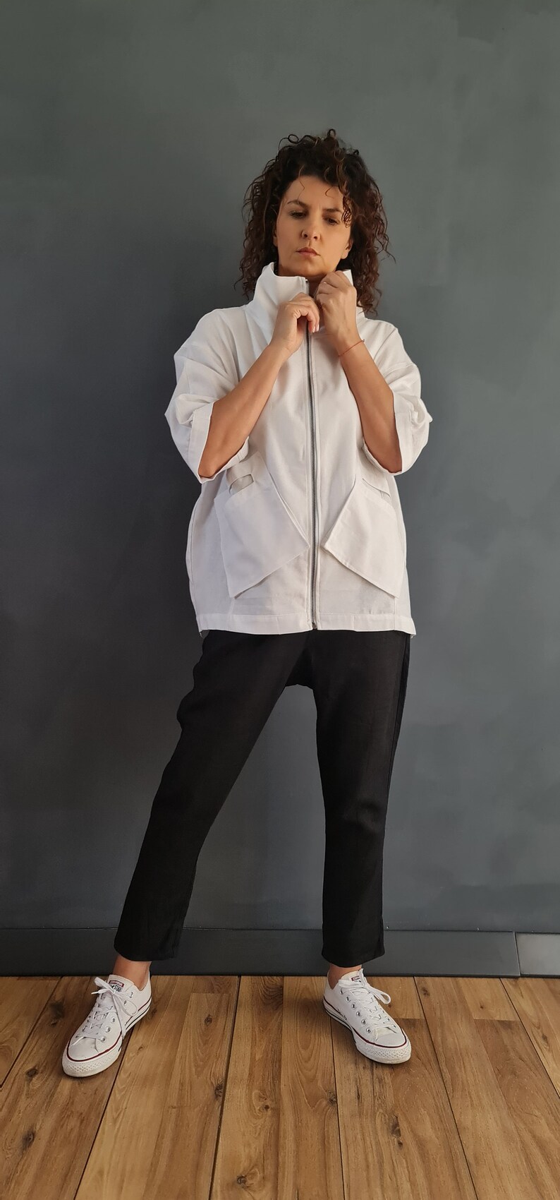 May include: A white zip-up jacket with a high collar and pockets. The jacket is worn over black pants and white sneakers.