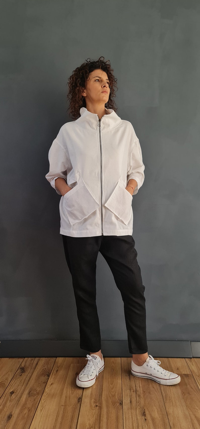 May include: A white zip-up jacket with large pockets and a high collar. The jacket is worn over black pants and white sneakers.